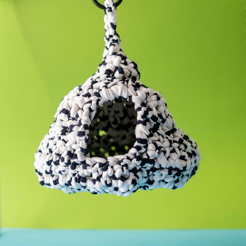 Ninho Azul e Branco em crochet para roedores Casa para pássaros tricotada em branco e preto pendurada com fundo verde.