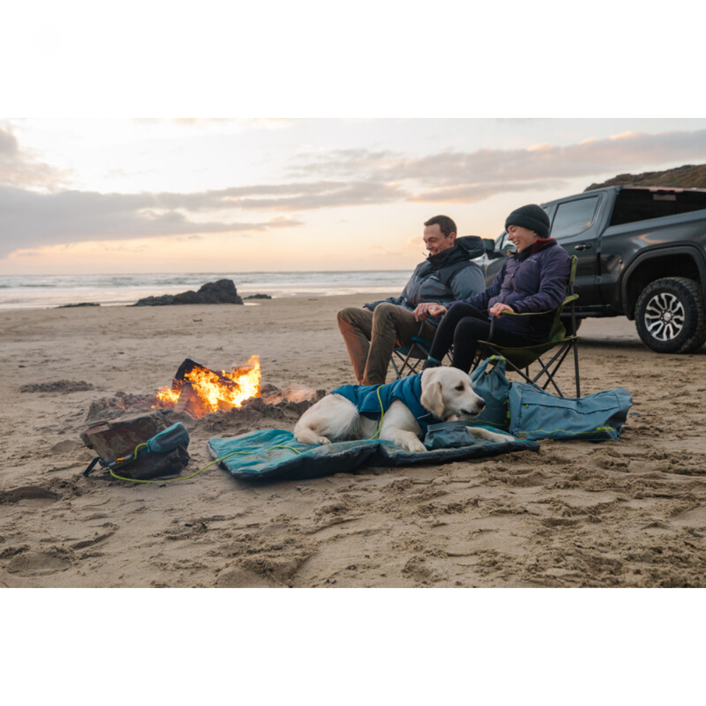 Hitch Hiker™ Leash - Aurora Teal Casal sentado em cadeiras dobráveis na praia com cão ao lado e fogueira, ao entardecer