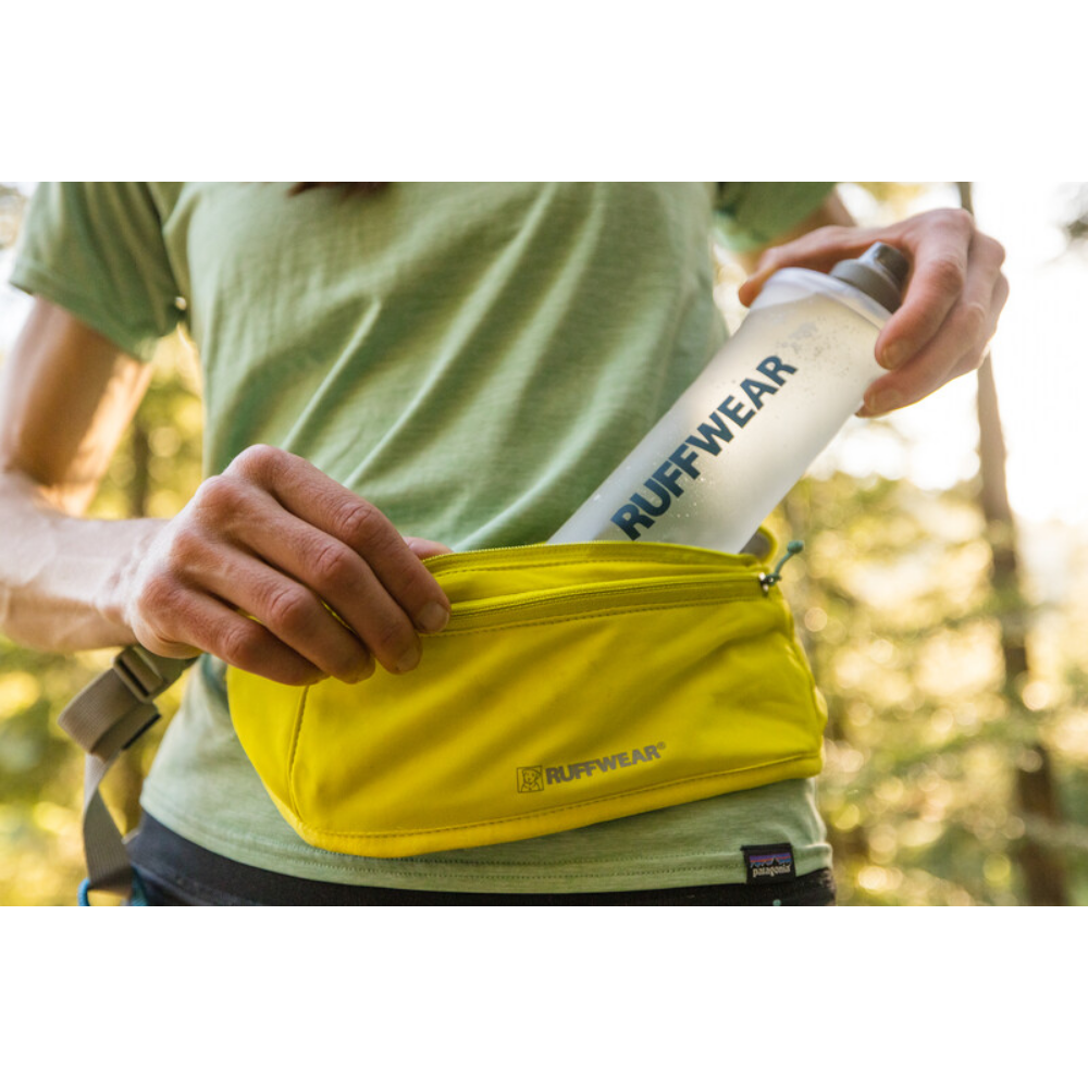 Trail Runner™ Running Belt - Lichen Green Pessoa a guardar garrafa RUFFWEAR em bolsa amarela ao ar livre