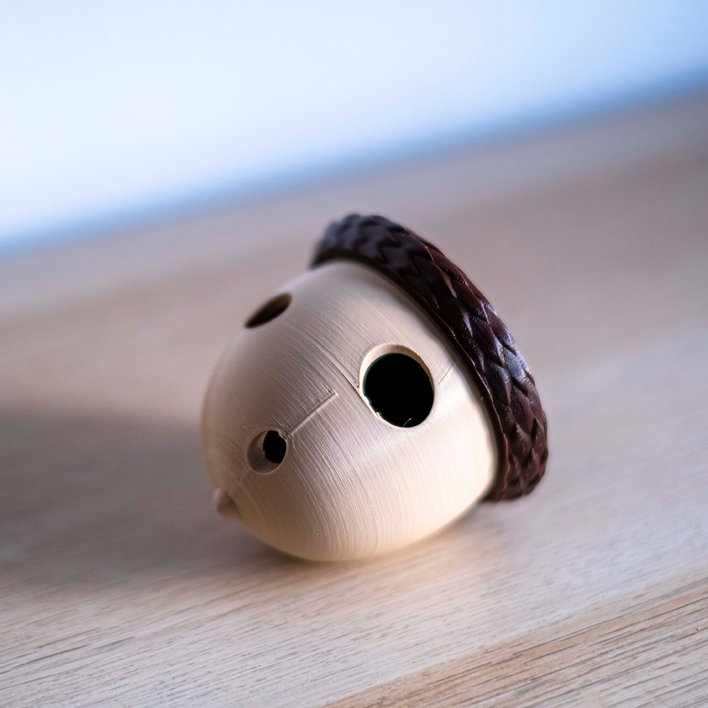 Rolling Acorn Objeto em forma de bolota com tampa marrom escura sobre superfície de madeira clara