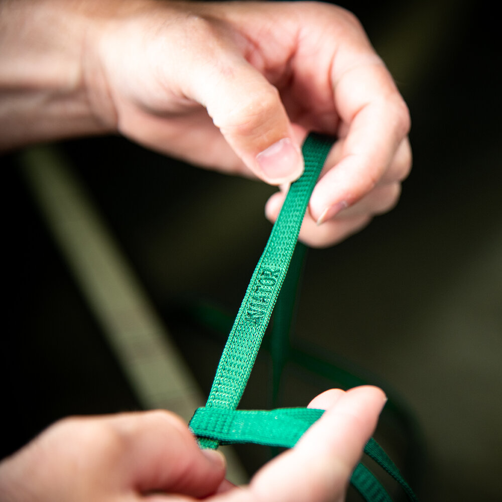 Aviator Vermelho - Bird Harness Fita verde de tecido com palavra 'STILO' segurada por duas mãos.