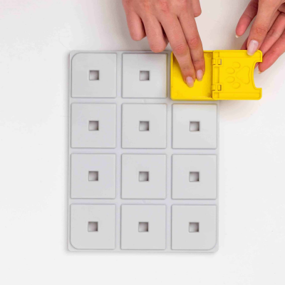 Base cinzenta com tampas amarelas, mão a abrir uma tampa com pegada.