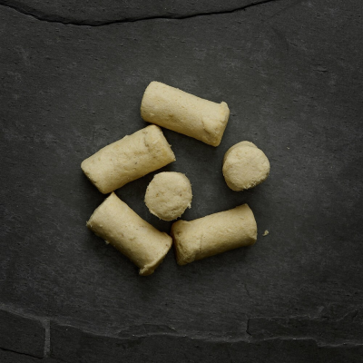 Petiscos beige esponjosos e cilíndricos sobre superfície escura de pedra.