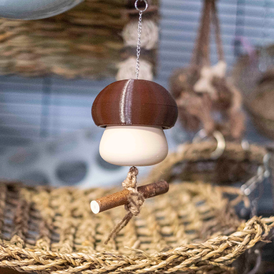 Pendente artesanal em forma de cogumelo com chapéu marrom e corpo branco, preso por corrente sobre fundo natural.