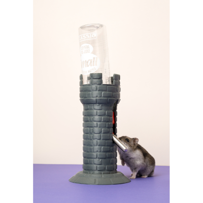 Dispenser para roedores em forma de torre cinzenta com garrafa transparente, rato a beber no bico, fundo branco e superfície roxa.