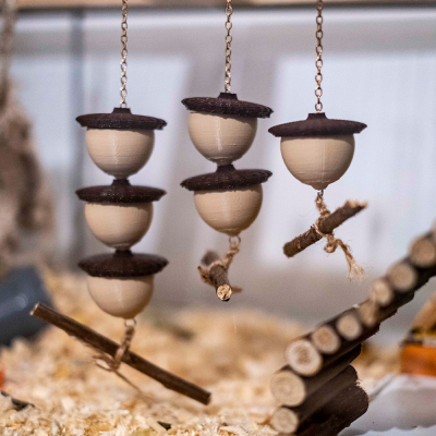 Trapézio suspenso para pequenos animais com bolas de madeira claras e discos escuros, varas de madeira e cordas em fundo de aparas de madeira.