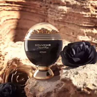 Frasco preto e dourado de perfume SOVENIR Desert Rose AFNAN sobre pedra com flores pretas e douradas