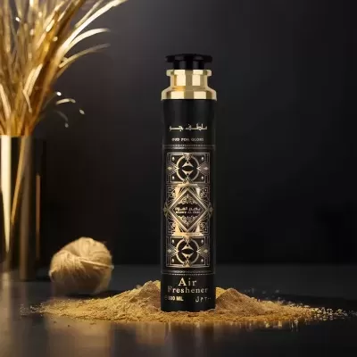 Frasco de ambientador preto com detalhes dourados sobre pó amarelo, com decoração dourada ao fundo