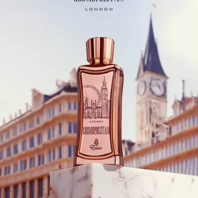 Frasco de perfume rosé com tampa dourada sobre base de mármore com edifícios ao fundo