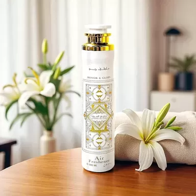 Frasco de aromatizador de ambiente branco e dourado com flores brancas ao lado numa mesa de madeira