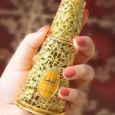 Frasco de perfume dourado com textura floral segurado por mão com unhas pintadas de rosa