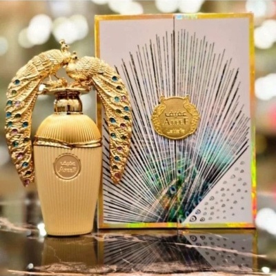 Frasco de perfume dourado com tampa decorada com aves e embalagem branca com detalhes dourados e penas de pavão