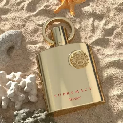Frasco de perfume dourado SUPREMACY AFNAN na areia com pedras e estrela-do-mar