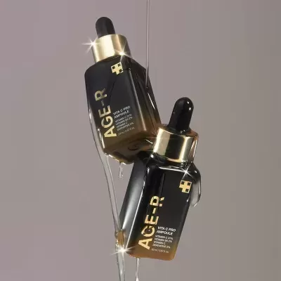Frascos de sérum AGE-R VITA C PRO AMPOULE com conta-gotas, detalhes dourados e fundo cinzento.