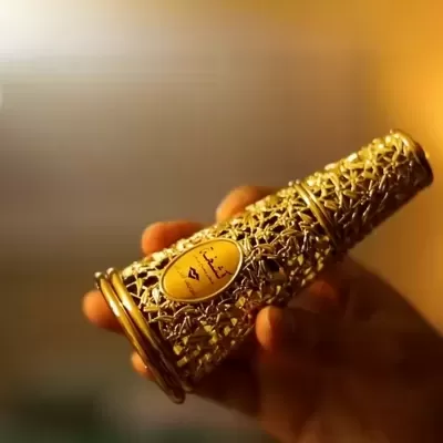 Frasco de perfume decorativo dourado com padrão rendilhado e rótulo em árabe