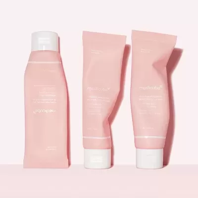 Três tubos cor-de-rosa de creme hidratante Medicube sobre fundo rosa claro