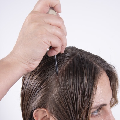 Mão a pentear cabelo castanho molhado com pente fino preto com cabo bege