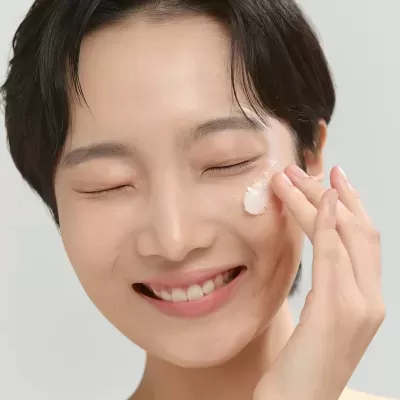 Mulher aplica creme branco no rosto sorrindo