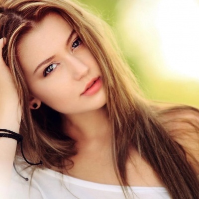 Mulher jovem com cabelo castanho claro e blusa branca em fundo desfocado verde