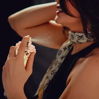 Pessoa a borrifar perfume num frasco transparente com líquido amarelo