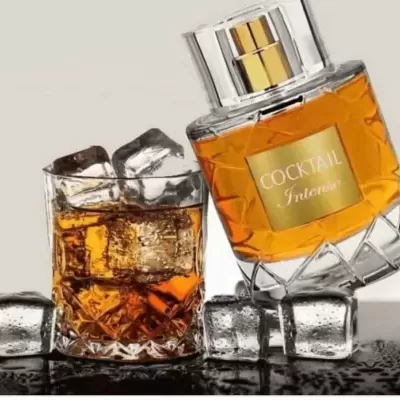 Frasco de perfume COCKTAIL Interiors ao lado de copo com líquido âmbar e cubos de gelo