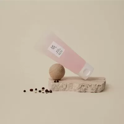 Tubo rosa translúcido com etiqueta em caracteres asiáticos a equilibrar em bloco de pedra com esfera de madeira e sementes.