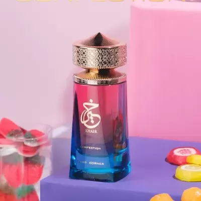 Frasco de perfume azul e rosa com tampa dourada sobre caixa roxa e doces ao redor