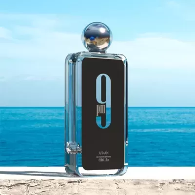 Frasco de perfume transparente com rótulo preto e líquido azul em fundo de oceano