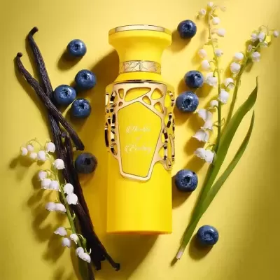 Frasco de perfume amarelo com detalhes dourados rodeado de mirtilos, vagens de baunilha e flores brancas