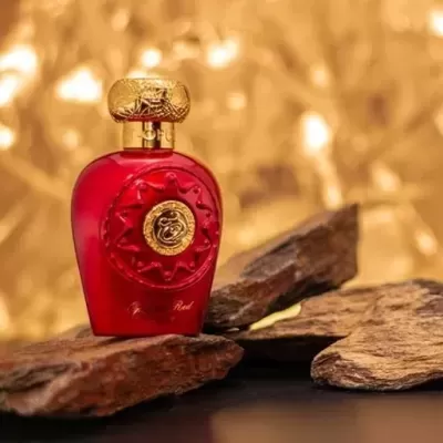 Frasco de perfume vermelho com detalhes dourados sobre madeira rústica