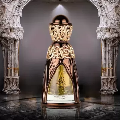 Frasco dourado e castanho de perfume com decoração ornamentada entre colunas de pedra branca