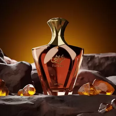 Frasco de perfume âmbar com tampa dourada sobre pedras âmbar e fundo alaranjado