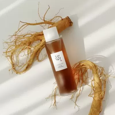 Frasco de Ginseng Essence Water e raízes de ginseng secas sobre fundo branco