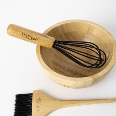 Utensílios de cozinha em madeira clara e silicone preto sobre superfície branca