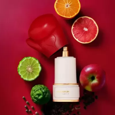 Frasco de perfume branco CHAMPION G.O.A.T com luva de boxe vermelha e frutas cortadas sobre fundo vermelho