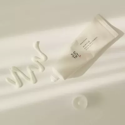 Tubo de creme branco aberto com creme aplicado em linha ondulada ao lado sobre superfície branca