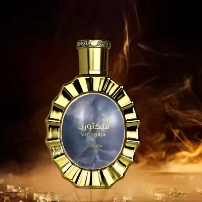 Frasco de perfume dourado com rótulo azul cinzento e texto VICTORIA em fundo esfumaçado