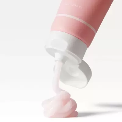 Tubo cor-de-rosa com tampa branca aberta a sair pasta creme rosa