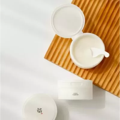 Pote branco de creme cosmético com espátula e tábua de madeira