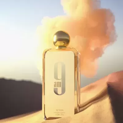 Frasco de perfume dourado com rótulo '9 am' em ambiente desértico