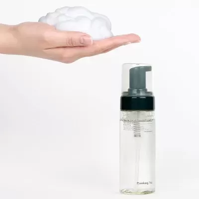 Frasco transparente com doseador de espuma e mão segurando espuma branca