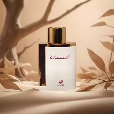 Frasco de perfume branco com tampa dourada e escrita vermelha num ambiente natural decorativo