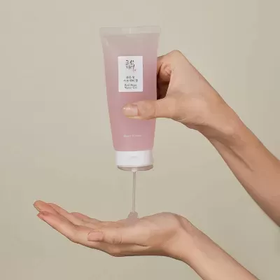 Frasco de gel líquido rosa sendo esvaziado em mão contra fundo neutro