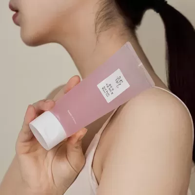 Frasco plástico rosa com tampa branca de gel cosmético na mão de mulher com fundo neutro