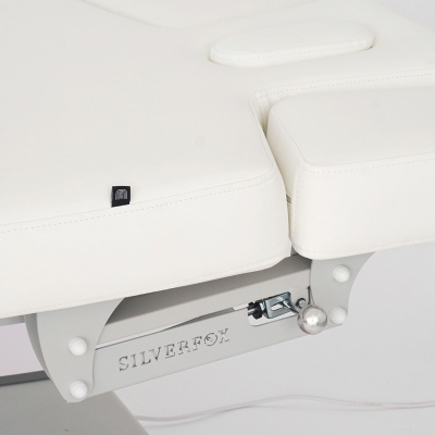 Cama de massagem branca com estrutura metálica cinzenta e etiqueta preta pequena