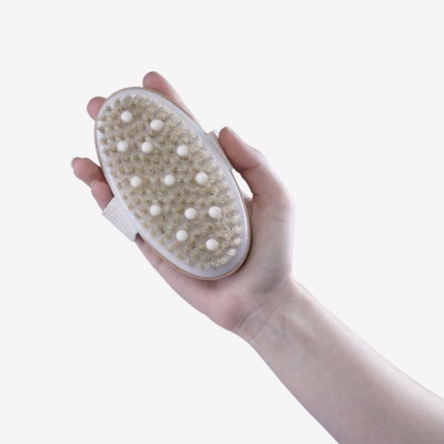 Escova de massagem corporal oval com cerdas naturais e bolinhas brancas numa mão