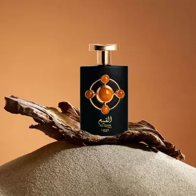 Frasco de perfume preto com detalhes dourados e âmbar sobre madeira e areia