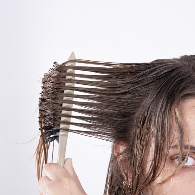 Pessoa a pentear cabelo molhado com escova preta de cerdas.