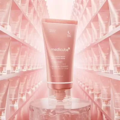 Tubo rosa do creme Medicube Collagen Night Wrapping Mask em pedestal transparente rodeado por tubos idênticos em prateleiras cor de rosa