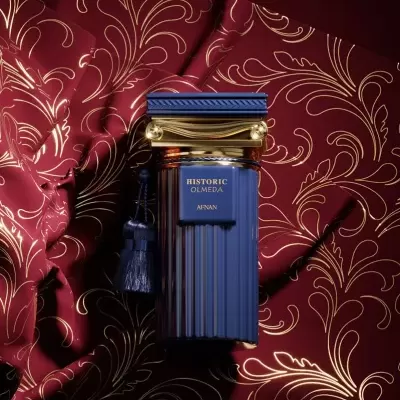 Frasco de perfume azul escuro com detalhes dourados sobre tecido vermelho com padrão dourado